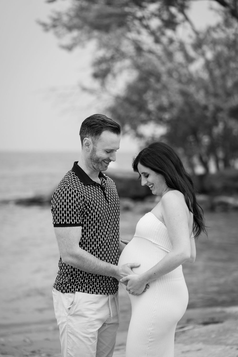 A couple shares an intimate moment by the water as they pose for their maternity photos in black and white.