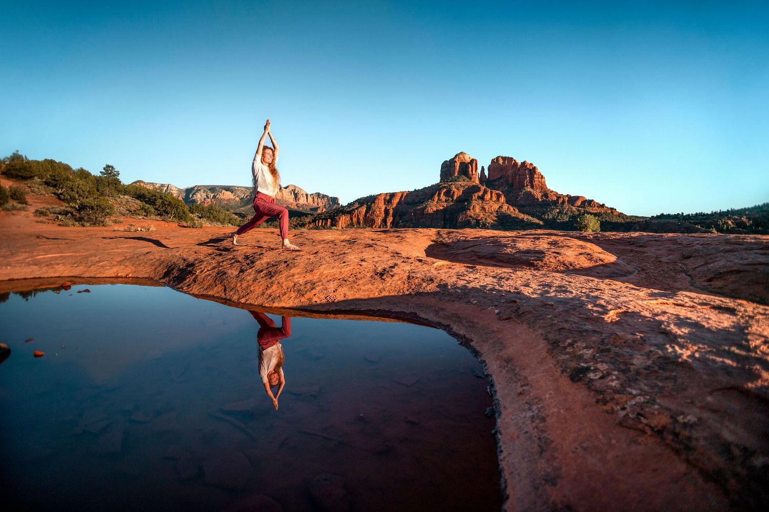 Yogi in tree pose reflected in still water pool surrounded by Sedona red rock formations.