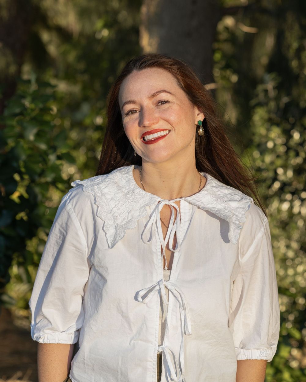 Woman smiling at the camera for an outdoor portrait. Beautiful greenery behind her. Professional branding and portrait