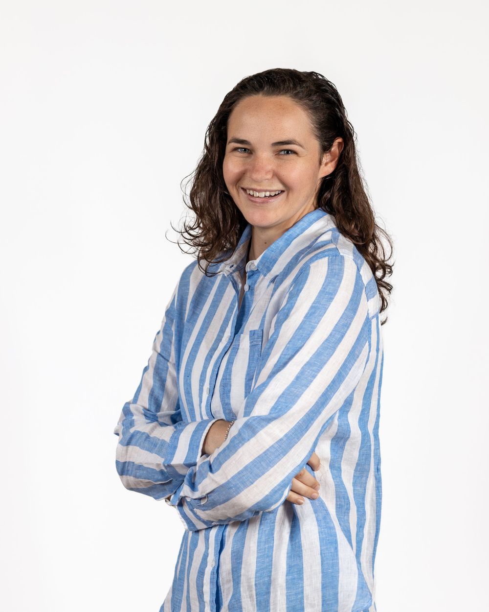 Professional Portrait of young lady with a bright big smile, standing with her arms crossed, wearing a white and blue striped shirt.