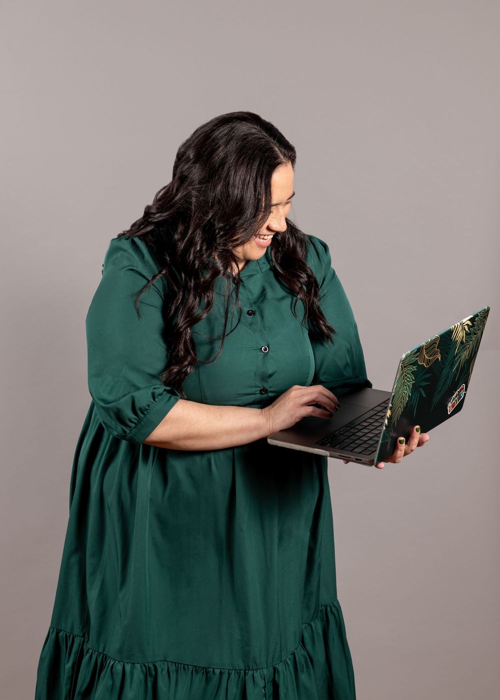 Pacific Island woman smiling looking down at her laptop while she type. Green dress, dark curly long hair. Branding portrait. CL Photography