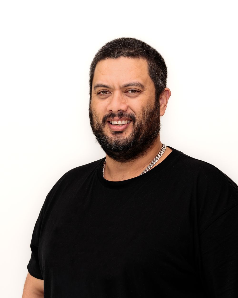 Studio Professional Headshot of Pacific Island male with a moustache and beard standing in front of a white background.
