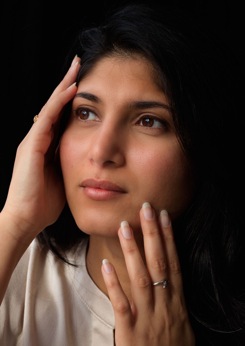 Close up of Indian woman's face looking away from the camera. Her face is framed by her hands. Editorial style portrait