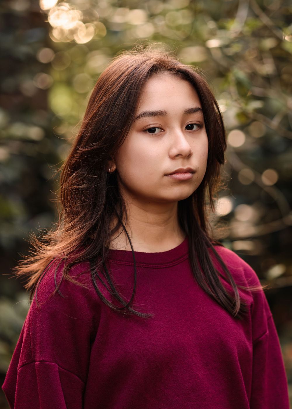 Professional headshot portrait of young Filipino woman taken outside with beautiful greenery bokeh in the background