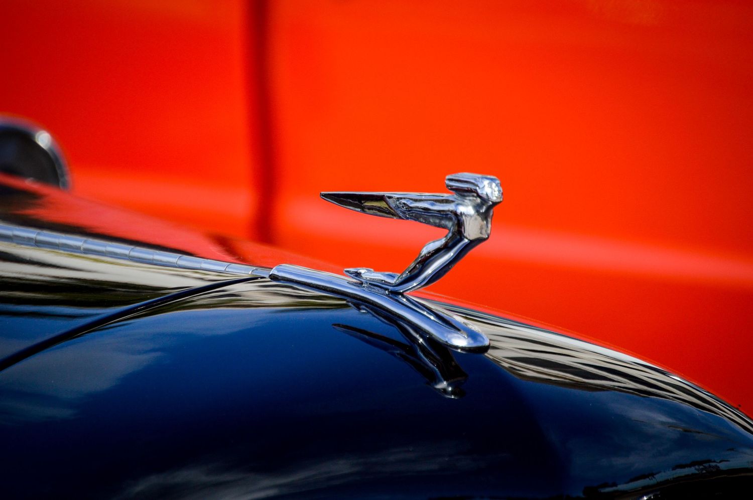 A classic chrome hood ornament from a Packard automobile stands out against a vibrant red and blue background.