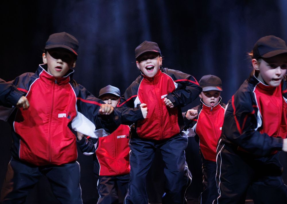 Group of performers in red jackets and black hats dance together during a theatrical stage production.