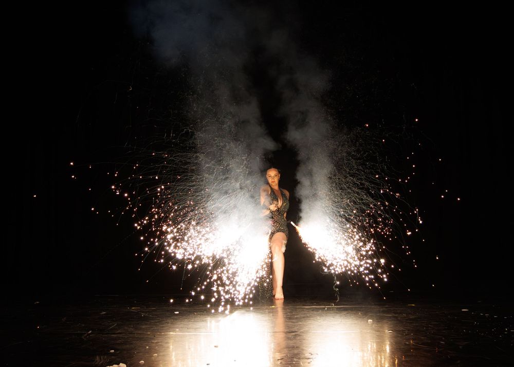 A person creates a dramatic light show effect with handheld sparklers against a dark night sky background.