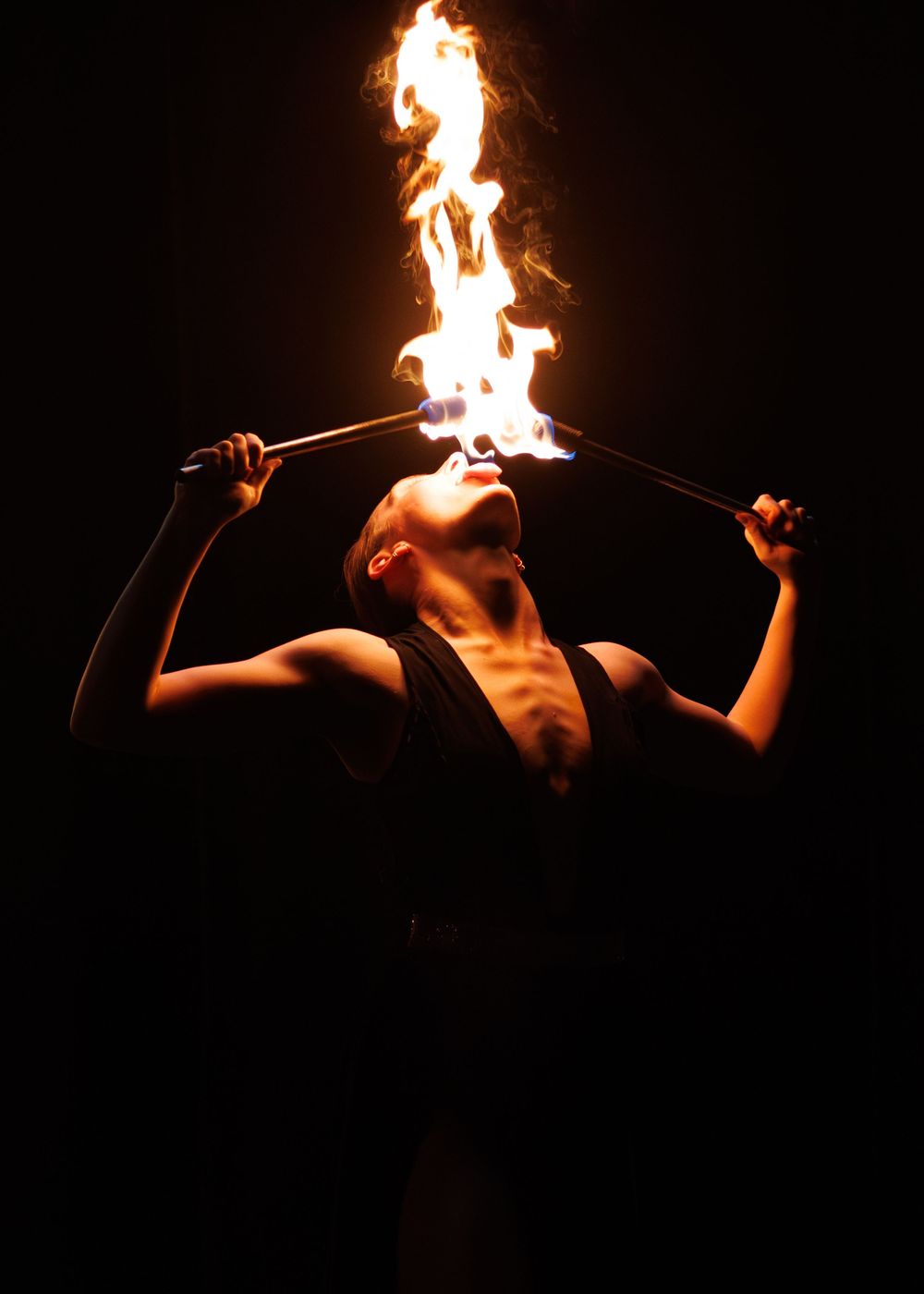 A performer breathes fire while arching backwards against a dark background in a dramatic display.