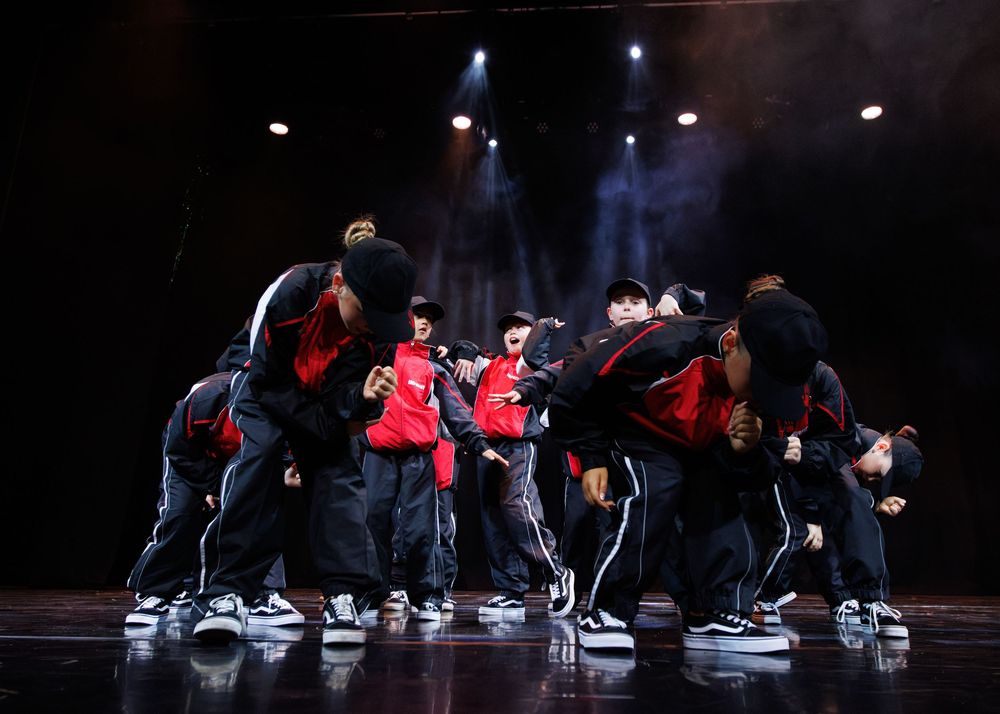 A synchronized dance crew performs an energetic hip-hop routine on a dimly lit stage.