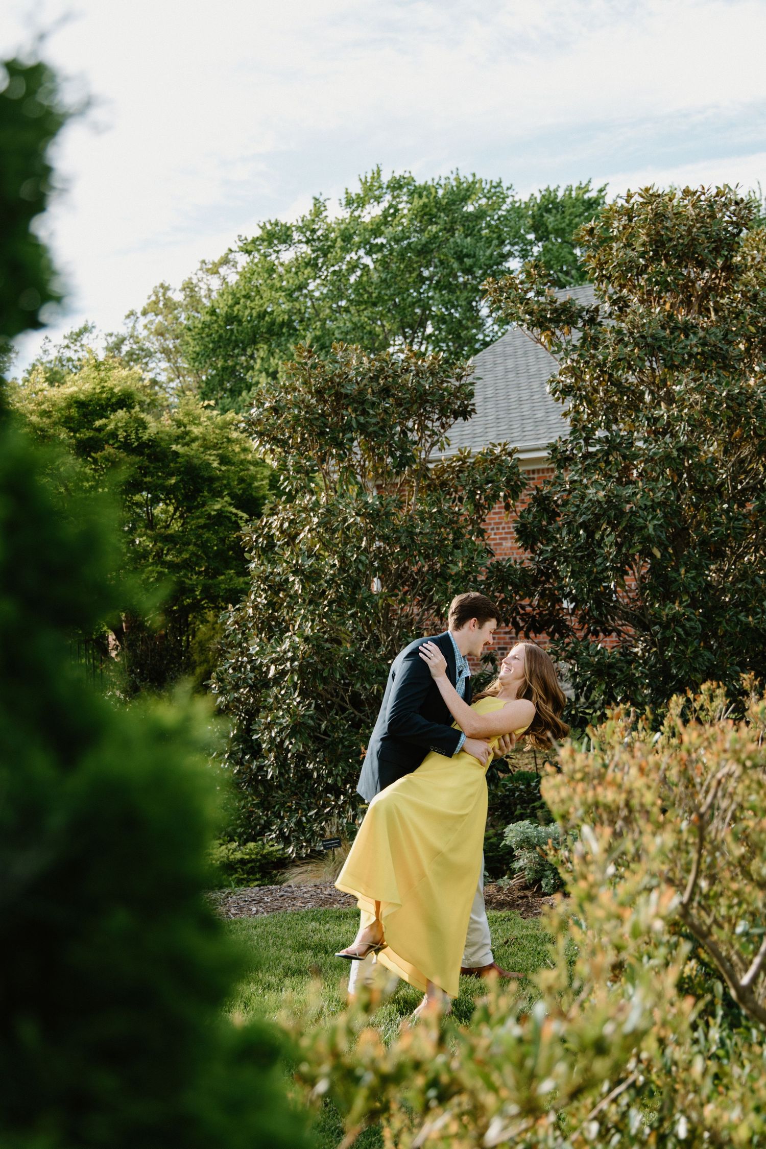 Two people share a romantic dance together among lush garden greenery on a sunny afternoon.