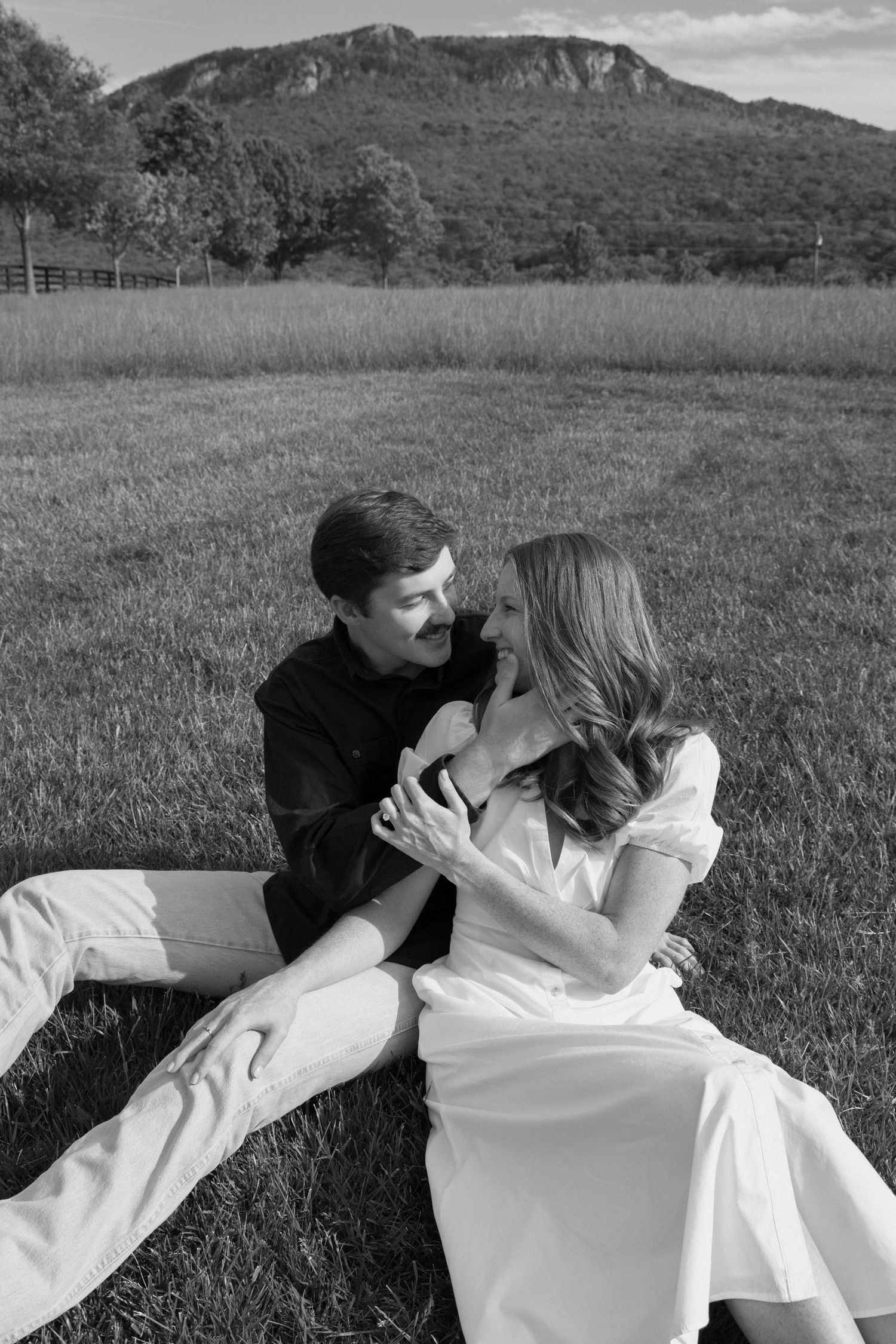 A couple shares an intimate moment in a serene meadow with mountains in the backdrop.