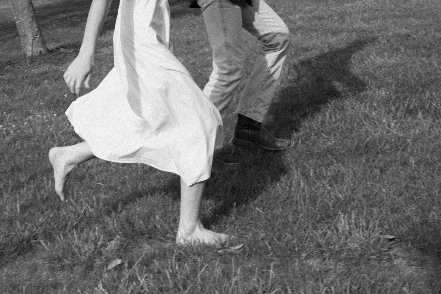 Black and white image of bare feet and flowing white dress fabric in motion on grass.