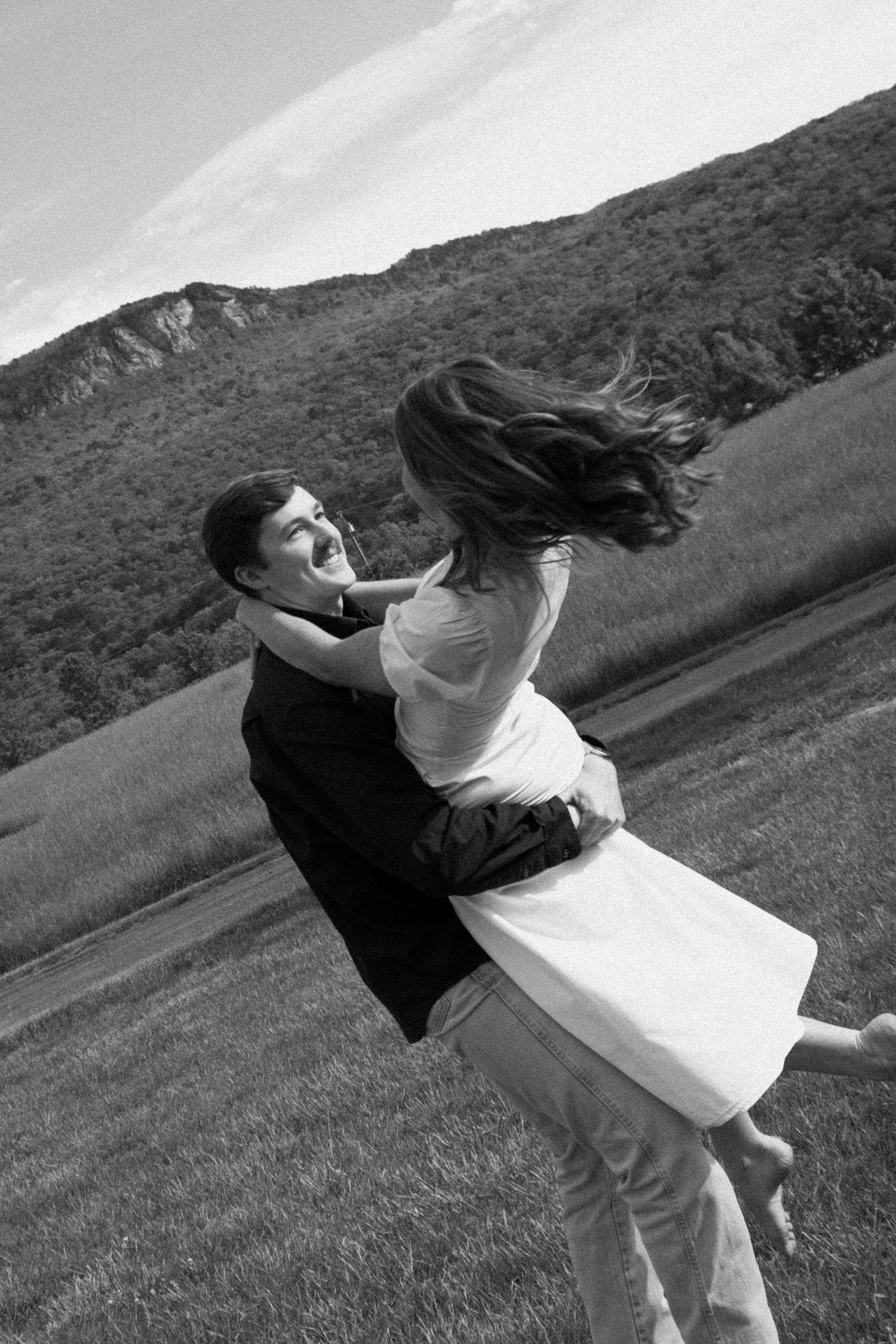 A romantic black and white photo of a couple embracing in a spinning dance move against a mountainous backdrop.