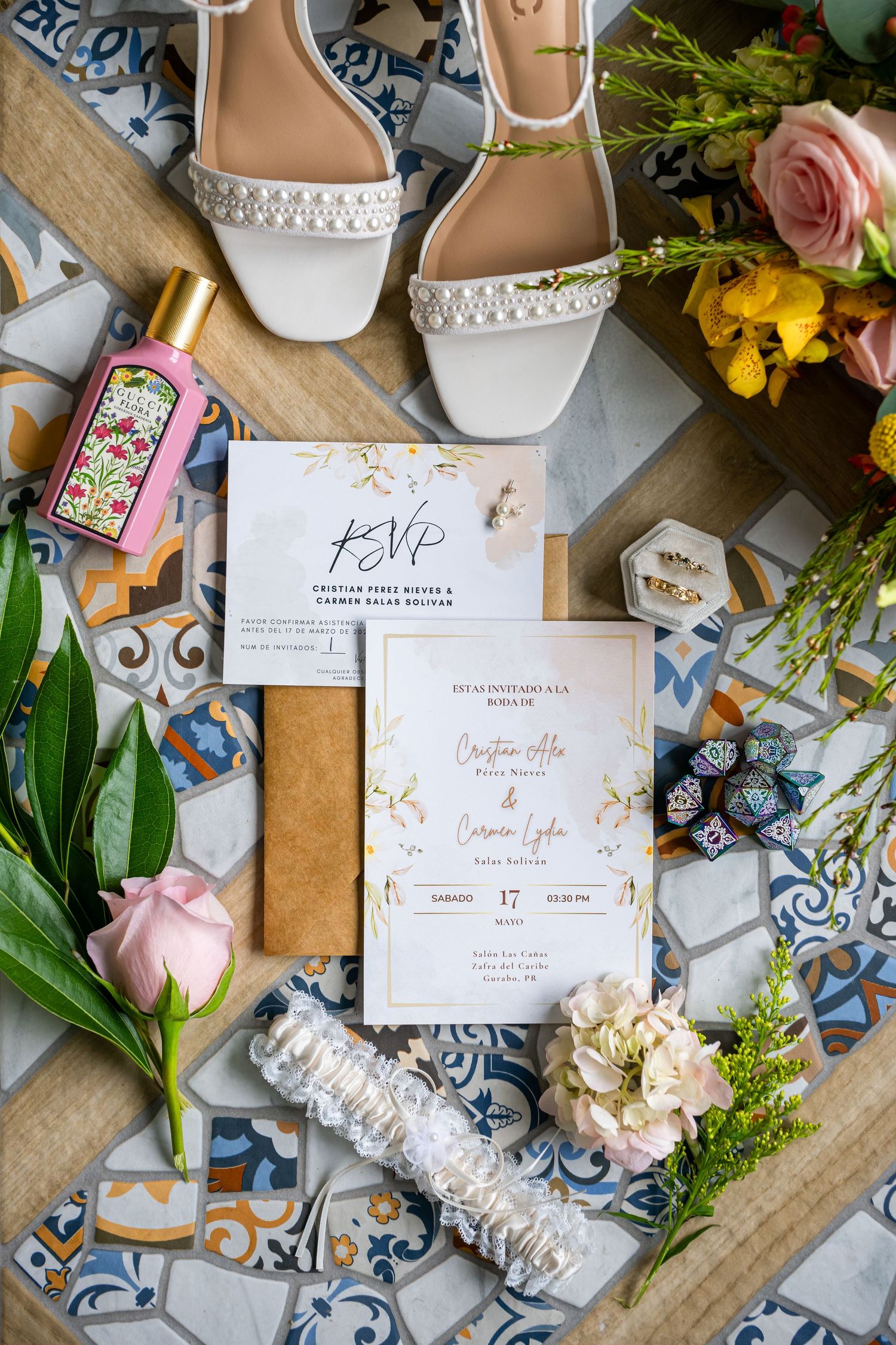 Wedding details flatlay showcasing bridal accessories, floral elements and RSVP invitation on vintage wooden and tile background.