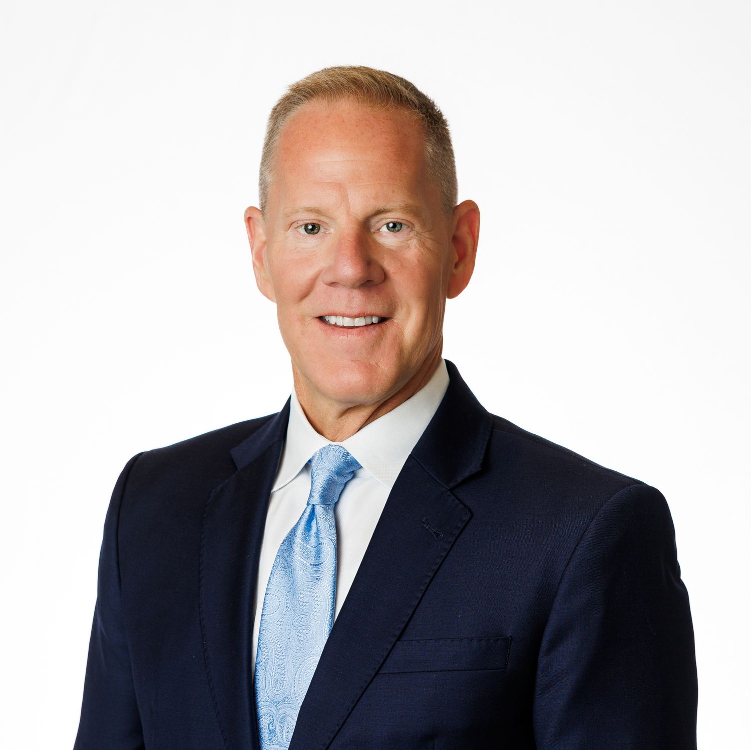 Professional headshot of someone in a navy suit and light blue tie against a white background.