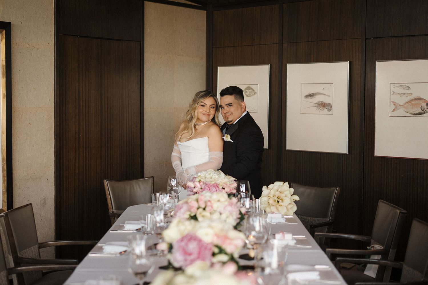 A panoramic view of wedding reception tables decorated with pink and white floral centerpieces in an elegant banquet room.