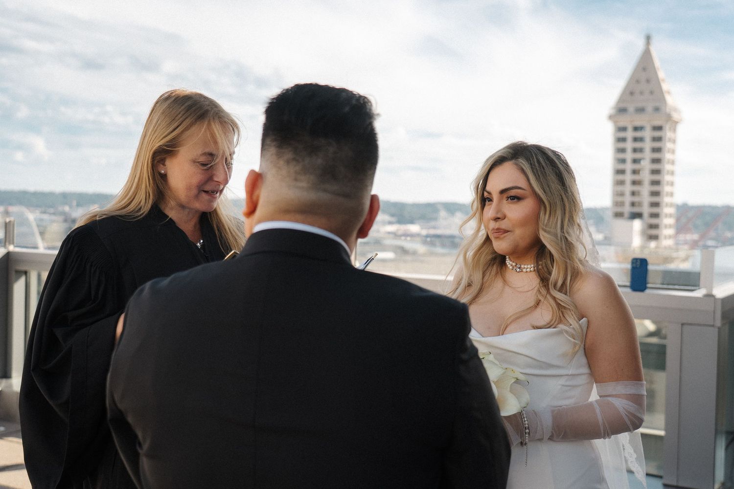 An intimate wedding ceremony takes place on a rooftop terrace with the Smith Tower visible in the Seattle skyline.