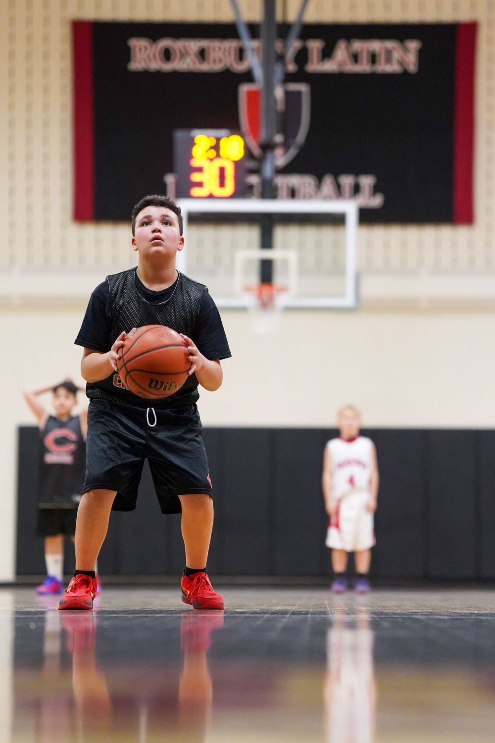 Youth basketball players in black uniforms practicing dribbling drills in a gymnasium.