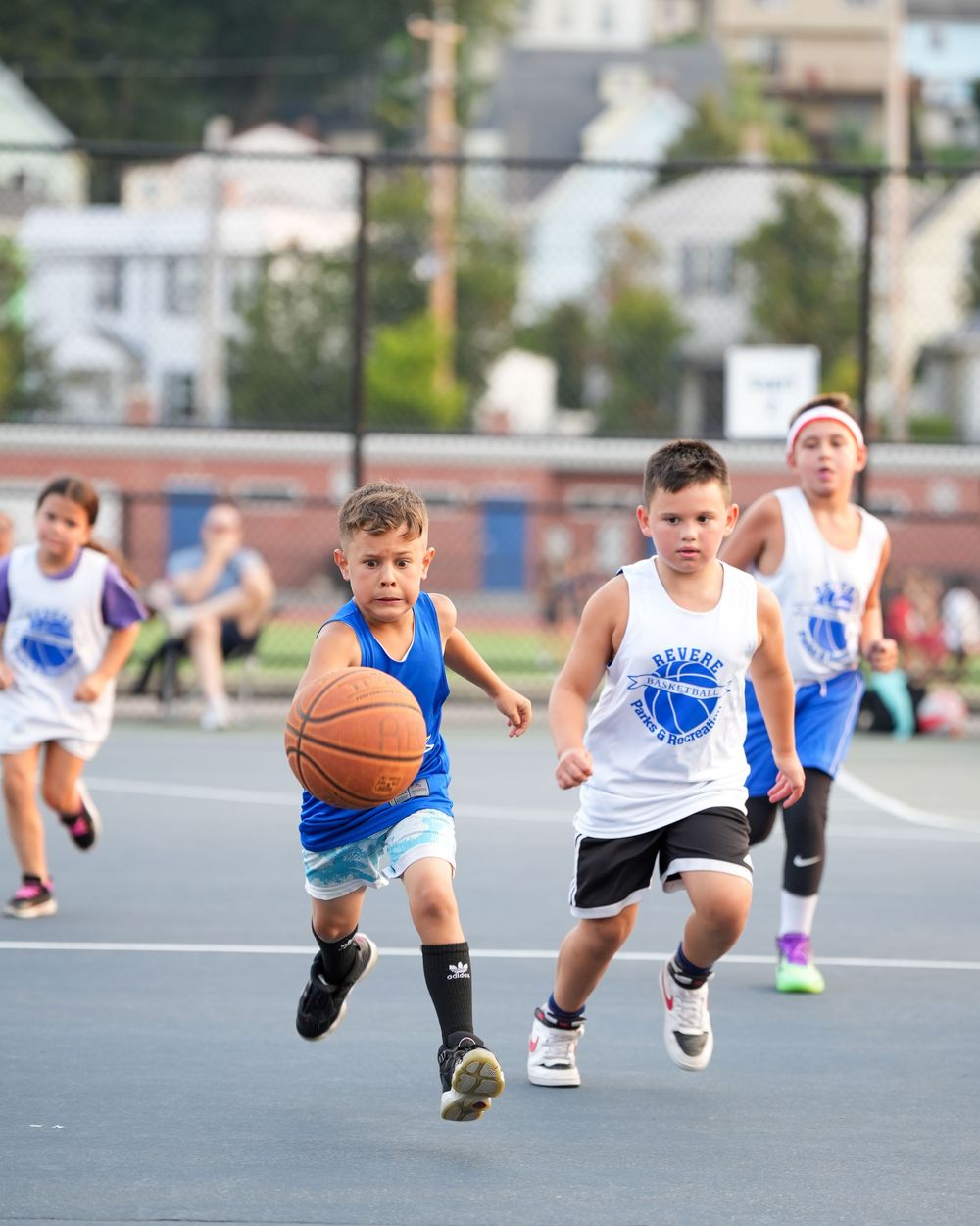 Young basketball players diving for a loose ball during an intense basketball practice drill on an outdoor court.