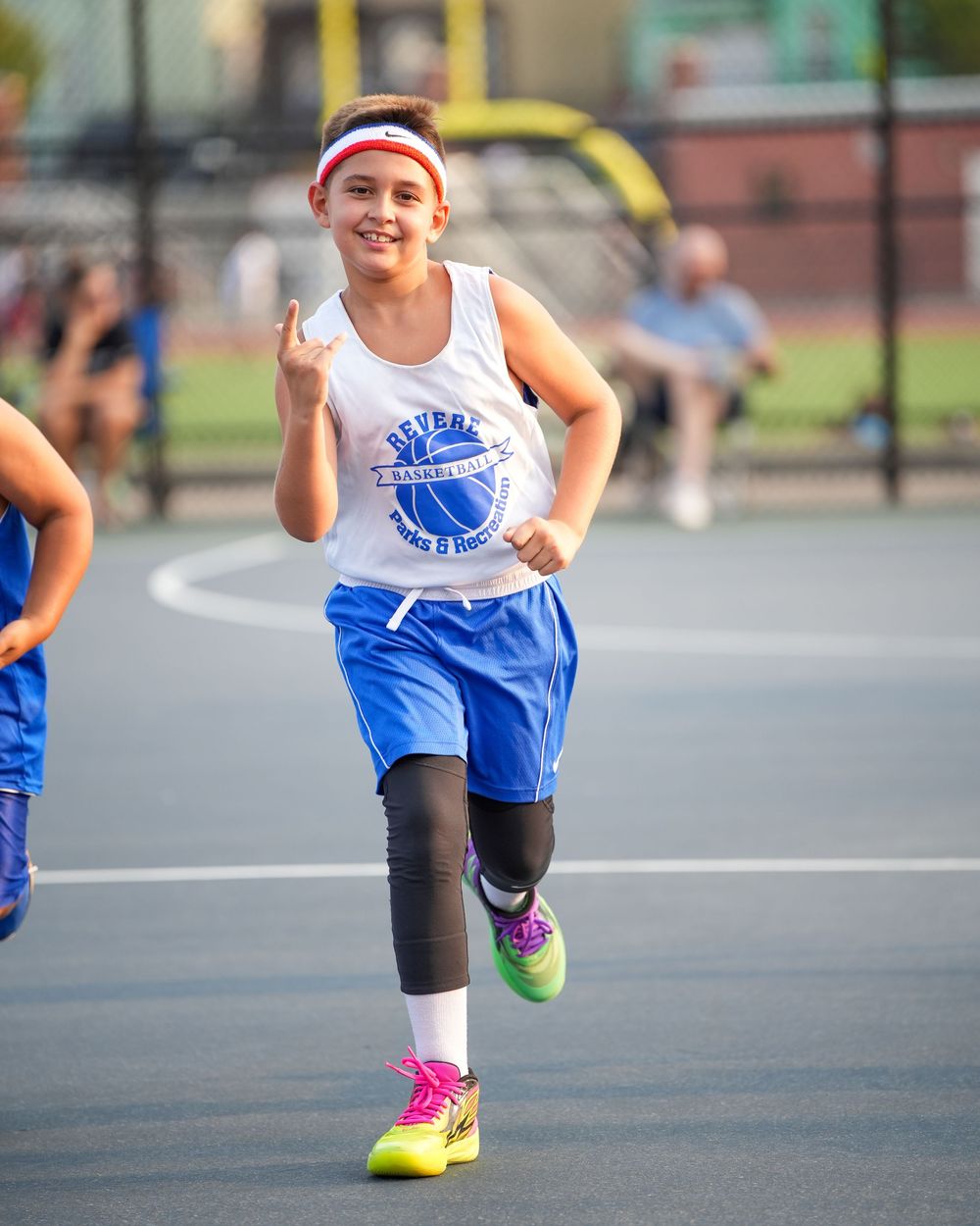 Young athlete in blue and white uniform running on basketball court wearing bright pink shoes and knee brace.