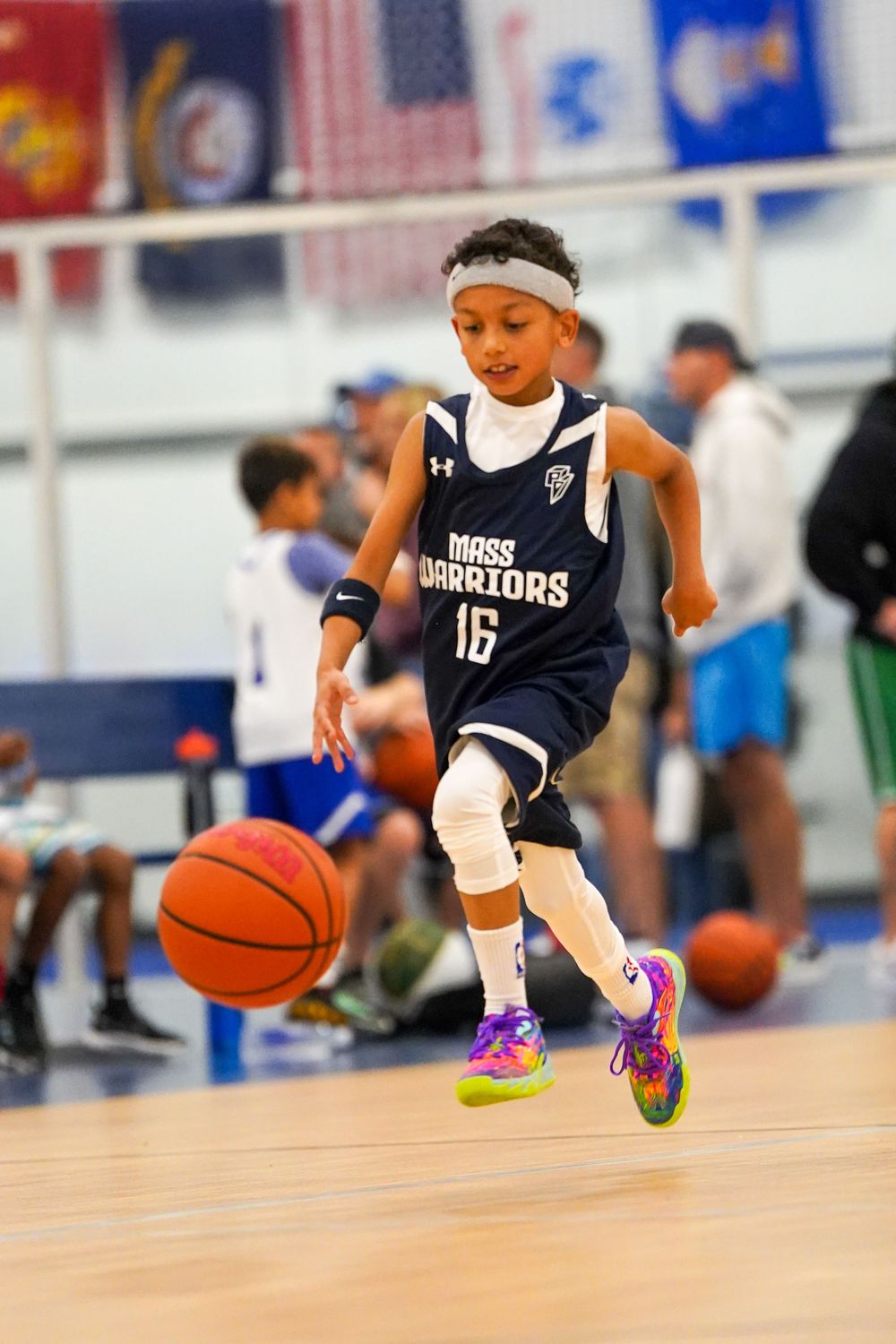 A child athlete diving low across a wooden basketball court floor to make a defensive play in a youth game.