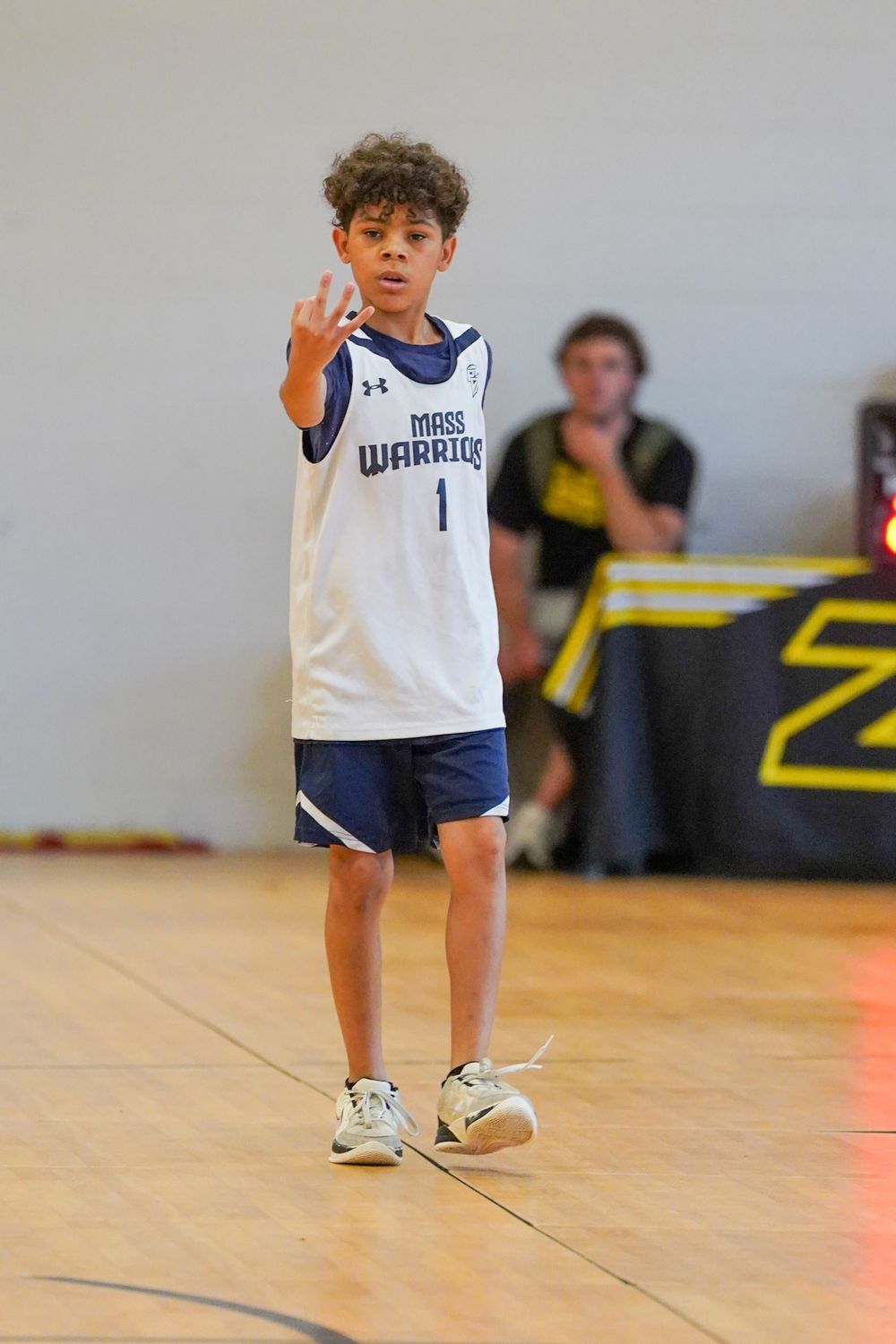 Young basketball player in white Warriors jersey number 1 gestures during a game in an indoor gymnasium.