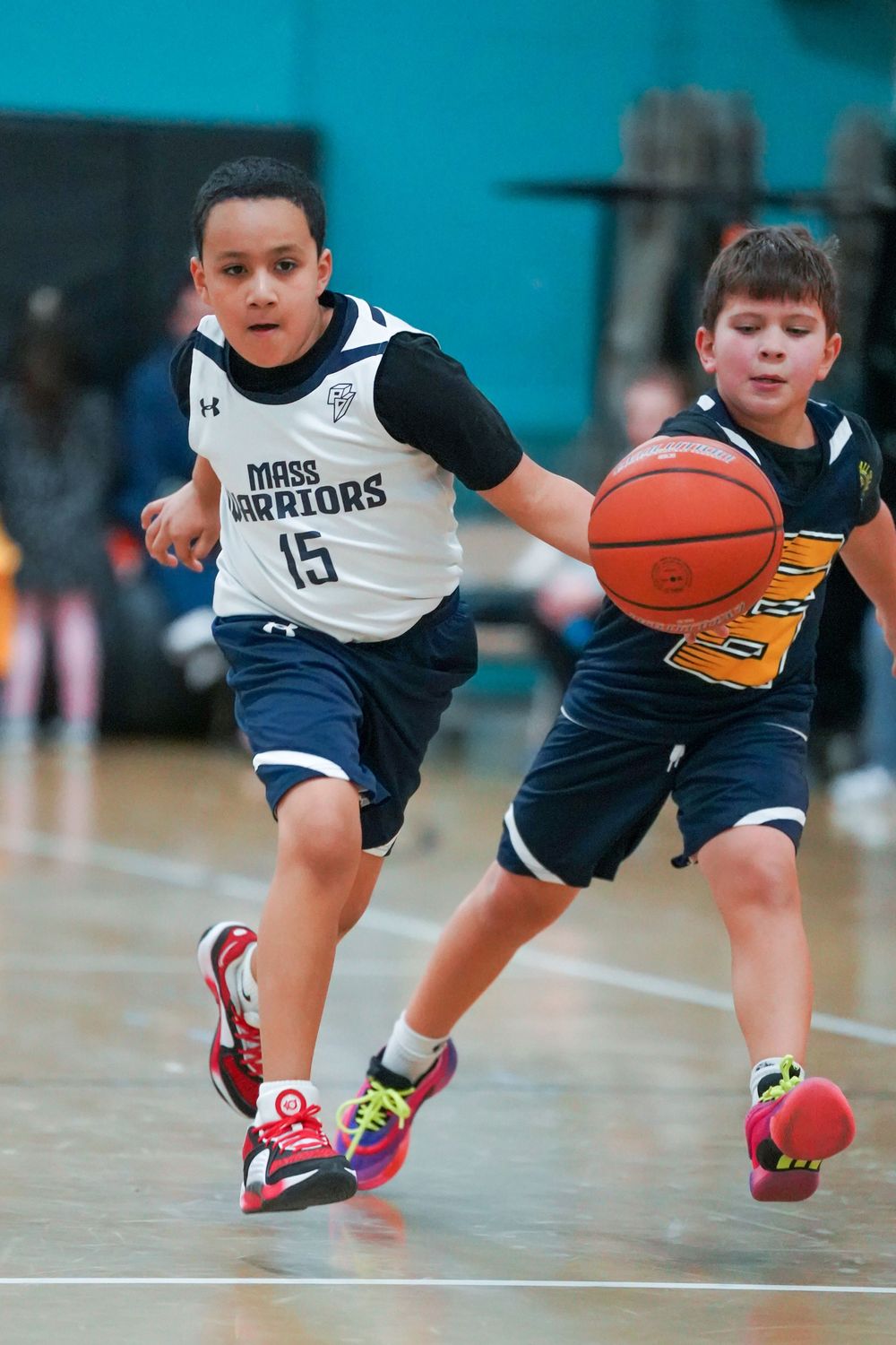Two young basketball players compete for the ball during a youth league game on an indoor court.