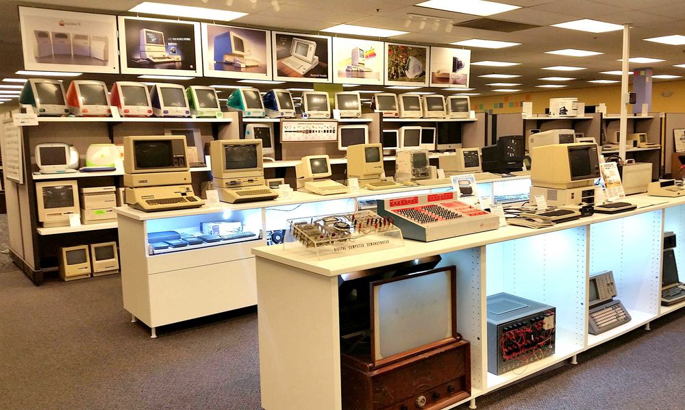 Vintage computer lab with rows of classic monitors and beige PCs displayed in a retail or museum setting.