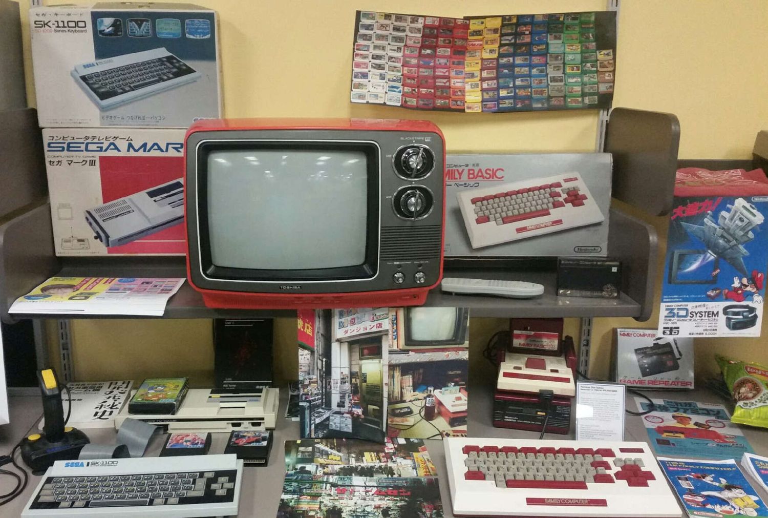 Vintage home computers and gaming consoles displayed on retail shelves with retro TVs and electronics items from the 1980s.