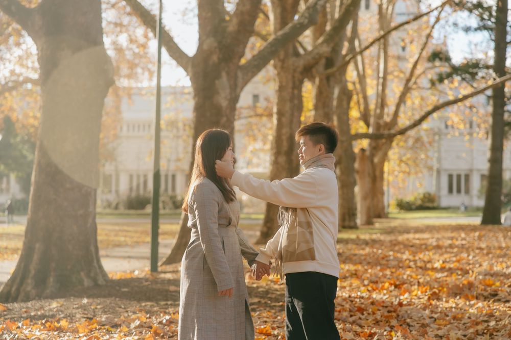 Couple sharing an intimate moment among autumn trees with fallen leaves on college campus grounds.