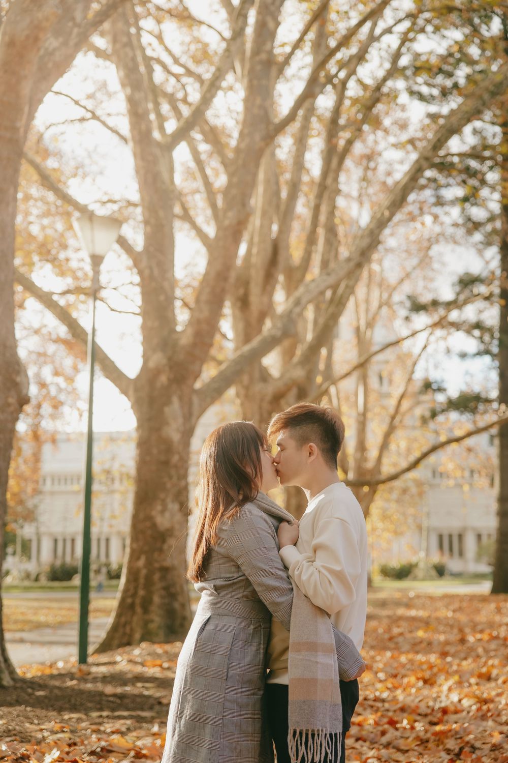 Romantic autumn engagement session in park with golden leaves and tall trees in background.