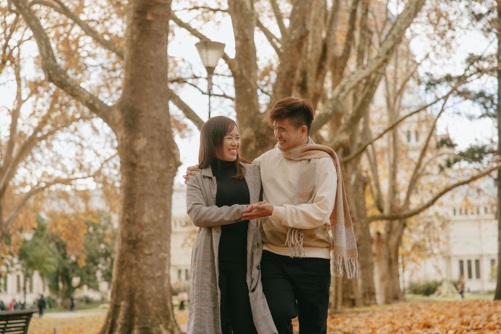 Couple in cozy sweaters enjoying autumn weather while walking through a tree-lined path.