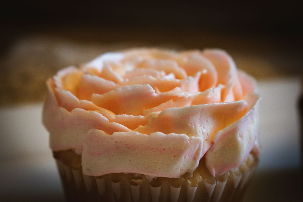 Soft peach-colored rose frosting swirls elegantly on a cupcake in macro view.