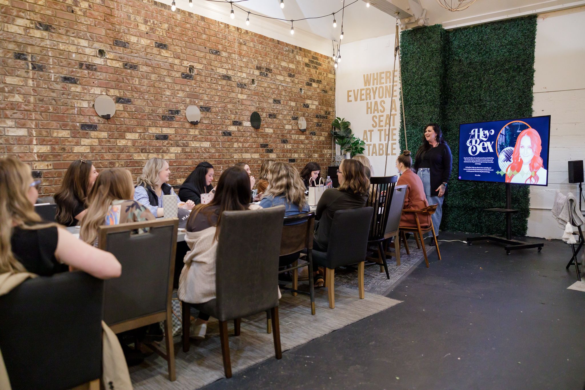EMPW women's networking community in Puyallup, WA woman standing at head of table with presentation slide deck to other women branding ed