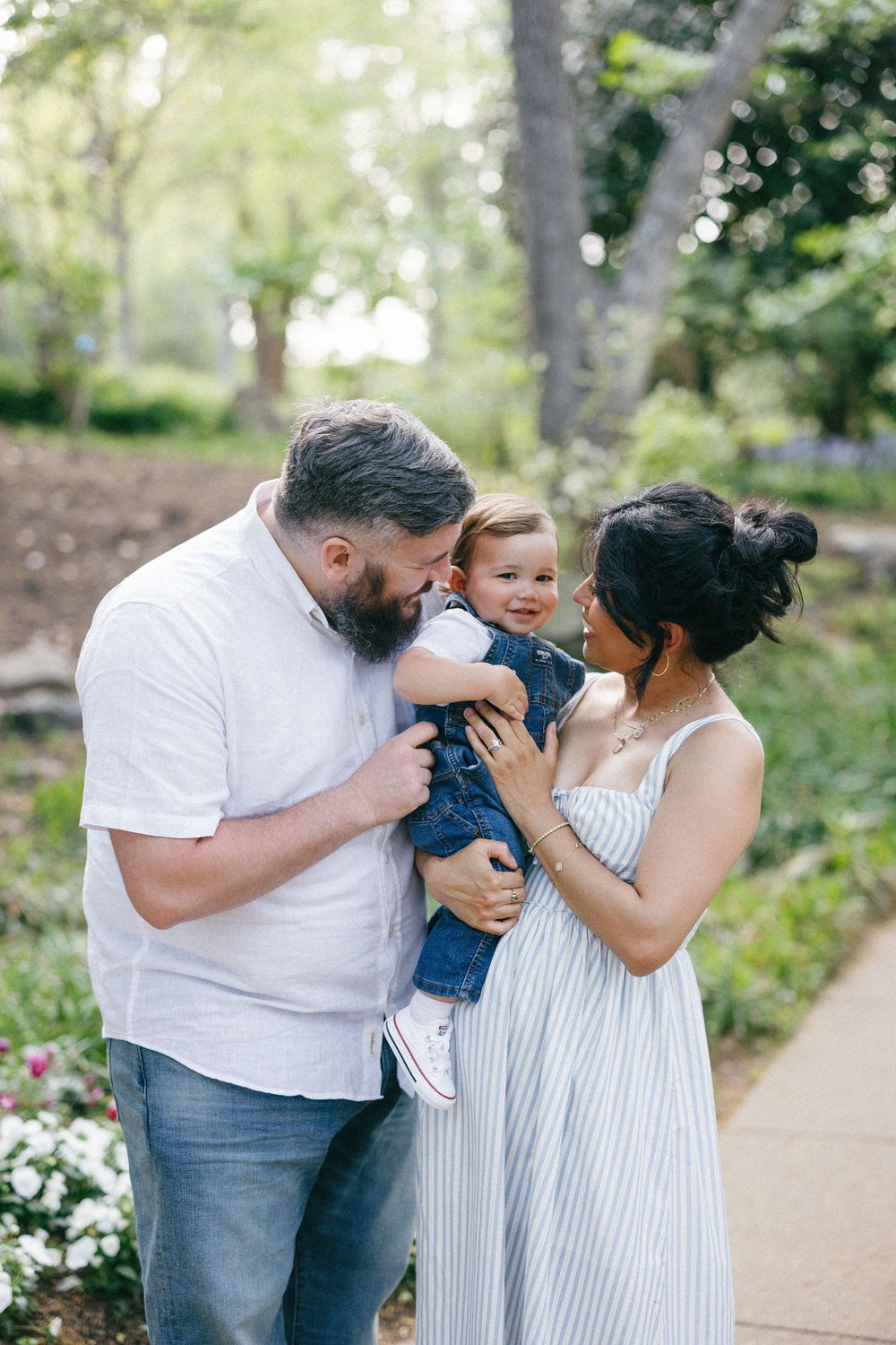 Family of three sharing loving kisses and hugs together on a scenic garden pathway.