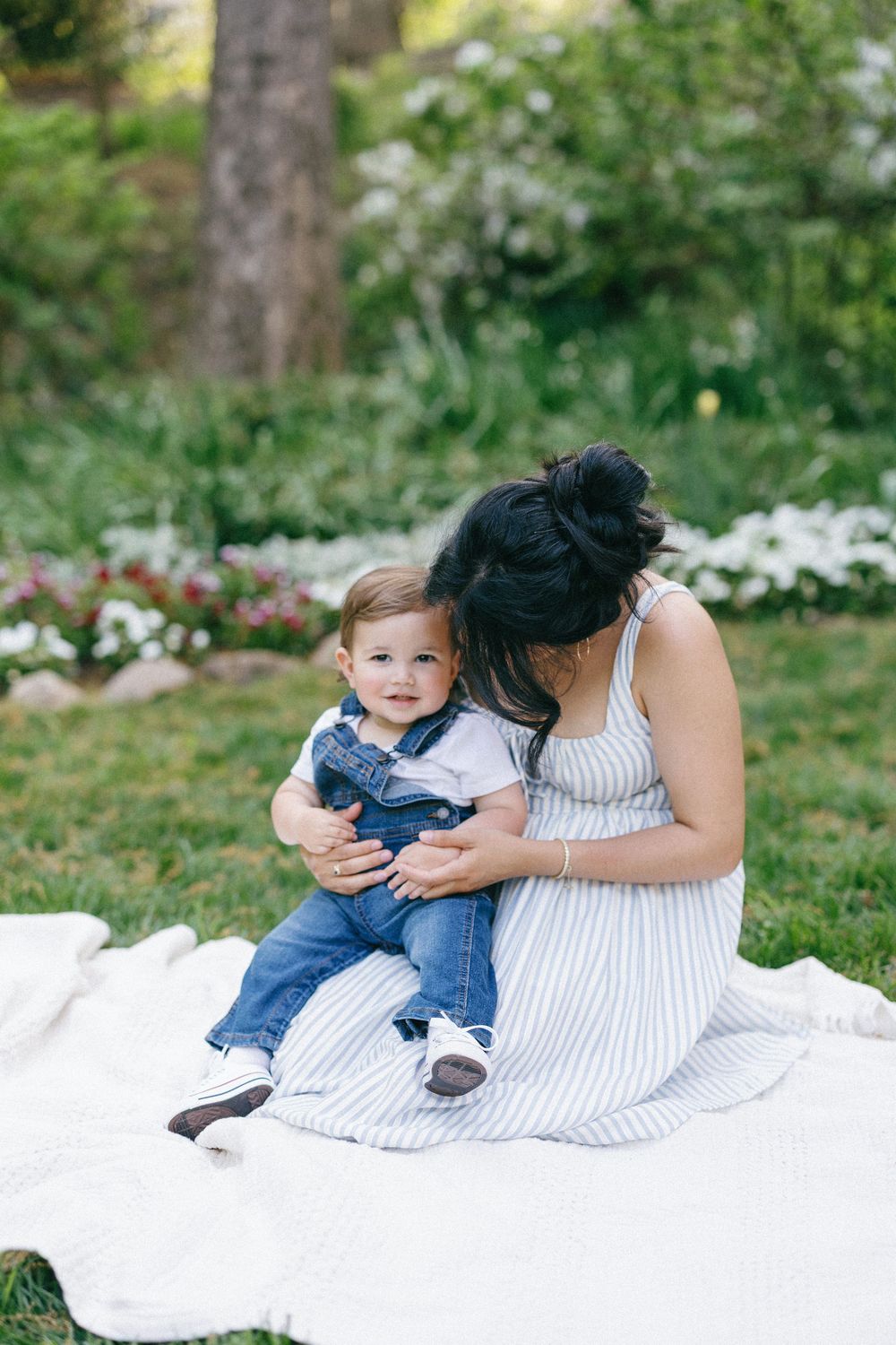 A tender outdoor photo session on a white blanket with denim and striped dress details in a garden setting.