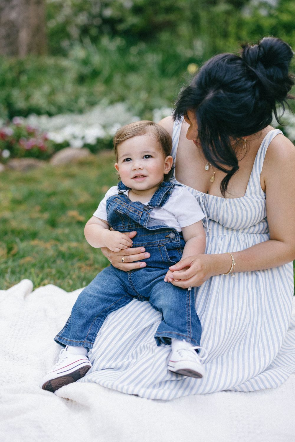A tender moment on a white blanket with a small child wearing denim overalls in a garden setting.