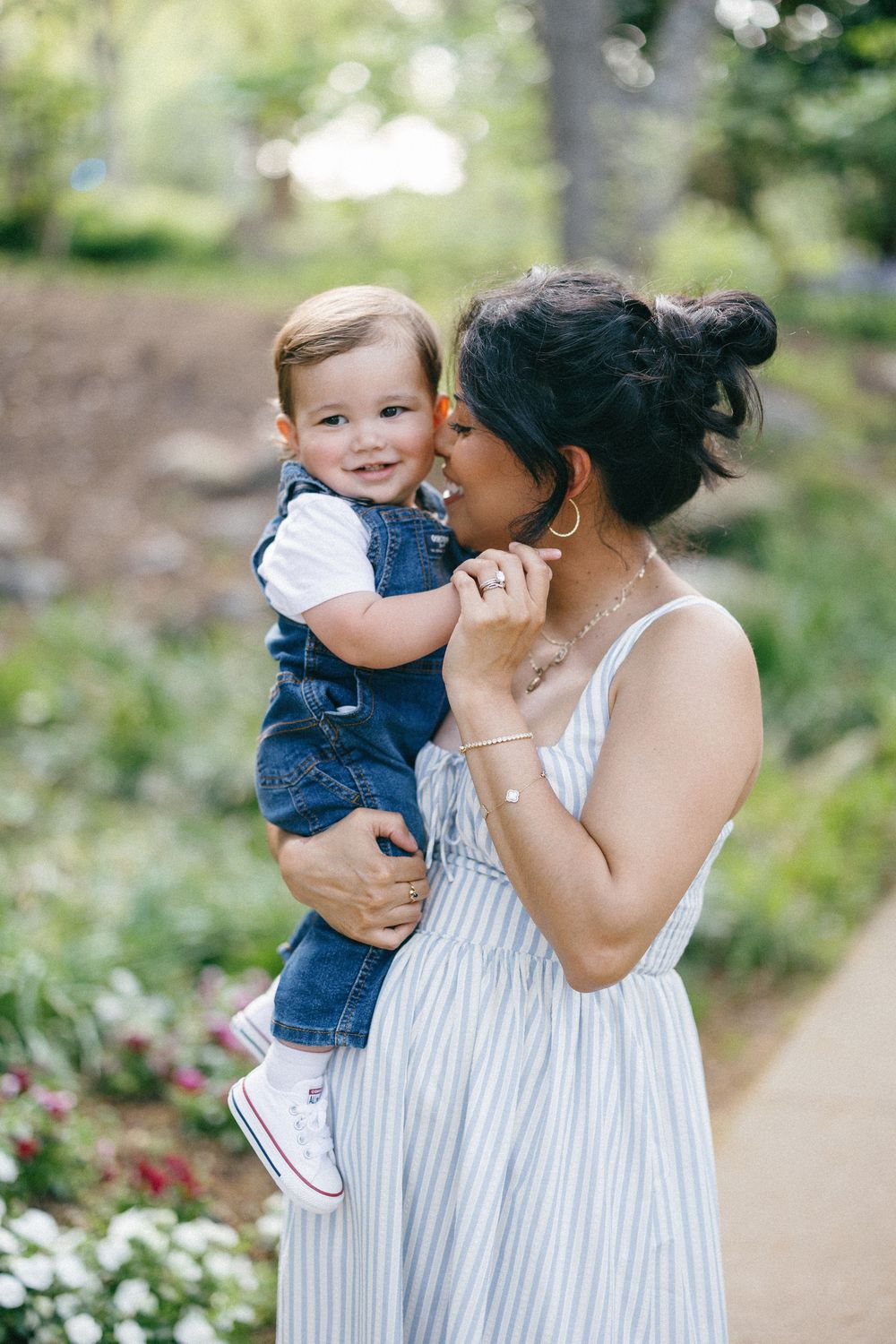 A tender moment between parent and child in striped dress and denim overalls in a sunlit garden path.