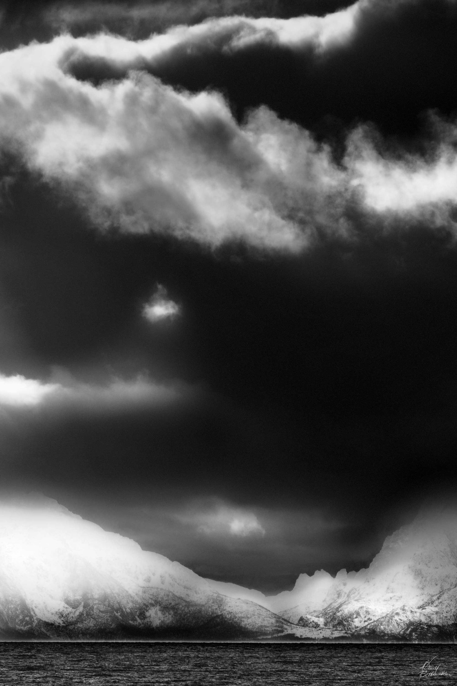 Dramatic black and white mountain landscape with stormy clouds and dark skies over snowy peaks.