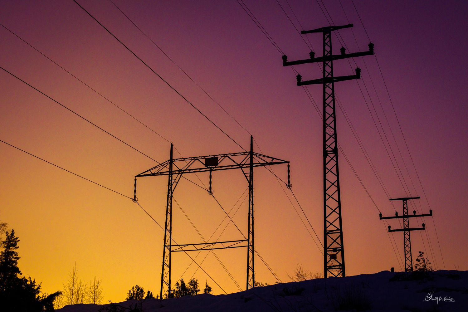Power lines and utility poles silhouetted against a vibrant purple and orange sunset sky.