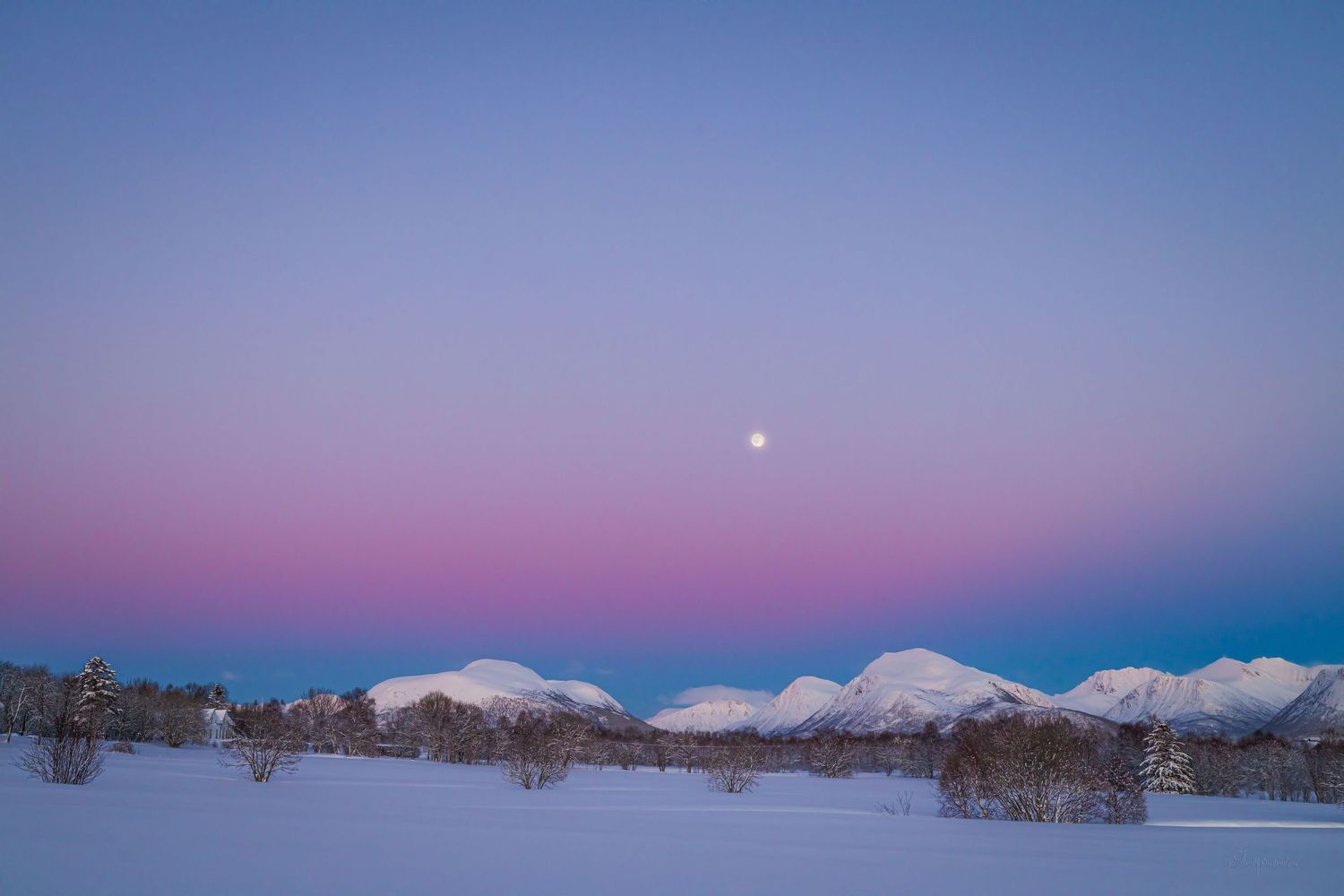 Snow-covered landscape at dusk with snow-capped mountains and a full moon rising in a purple and blue sky.