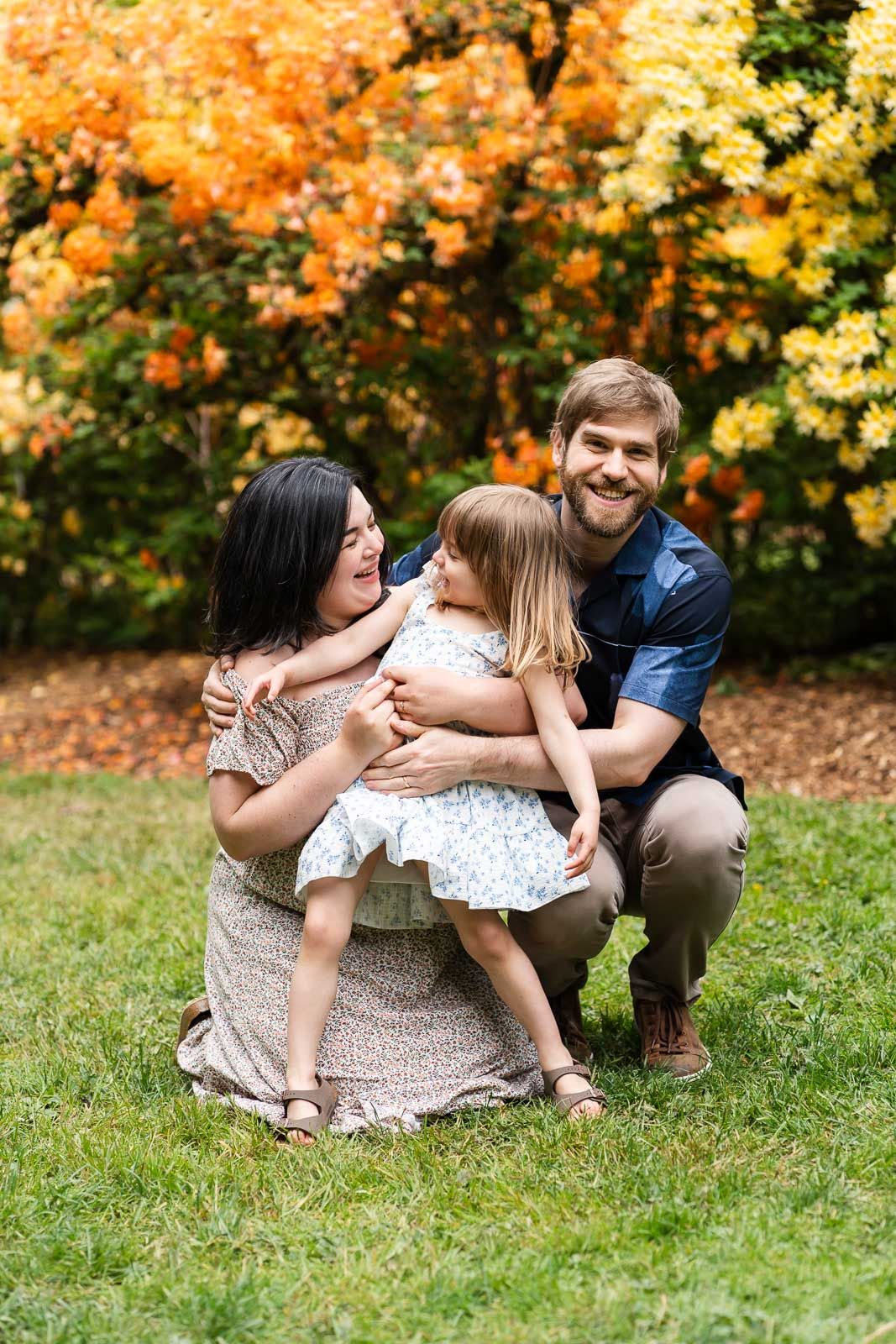 Family cuddling and smiling in front of the yellow and orange rhododendron flowers.