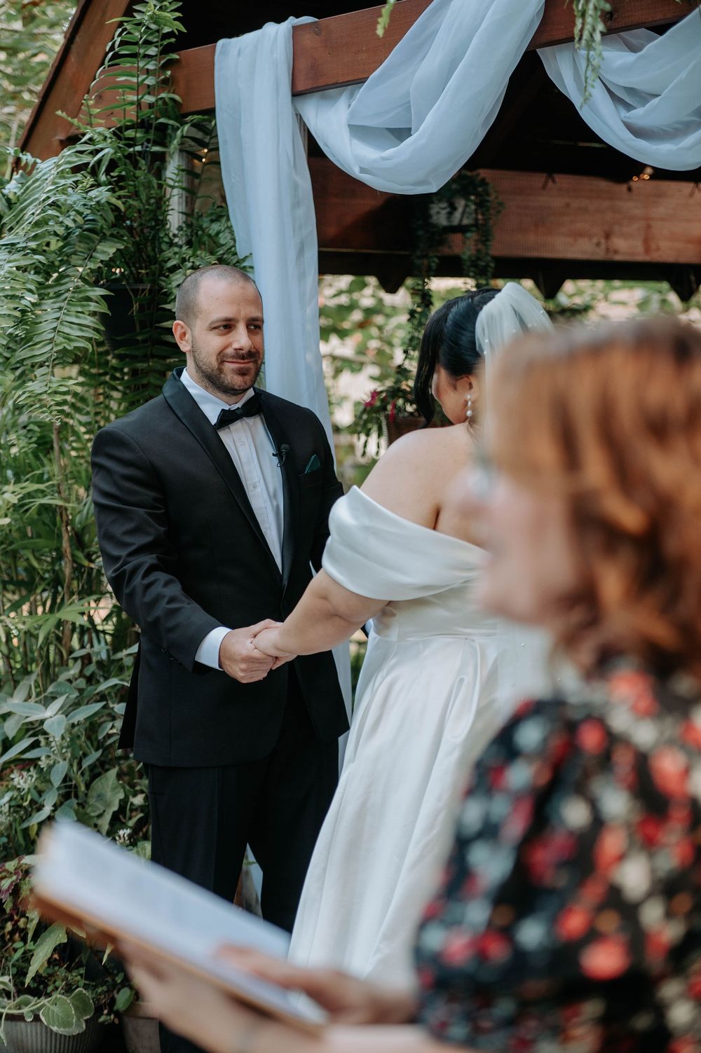 A romantic moment between a couple in formal attire surrounded by lush greenery and ferns.
