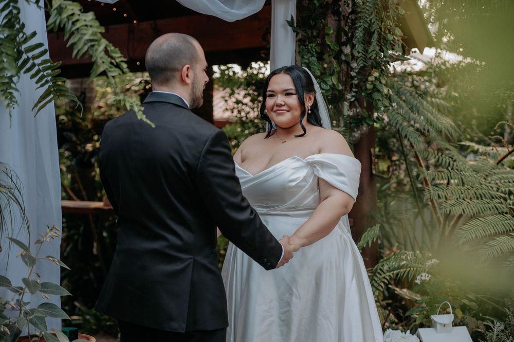 A tender moment between a couple in wedding attire surrounded by lush greenery at an outdoor ceremony.