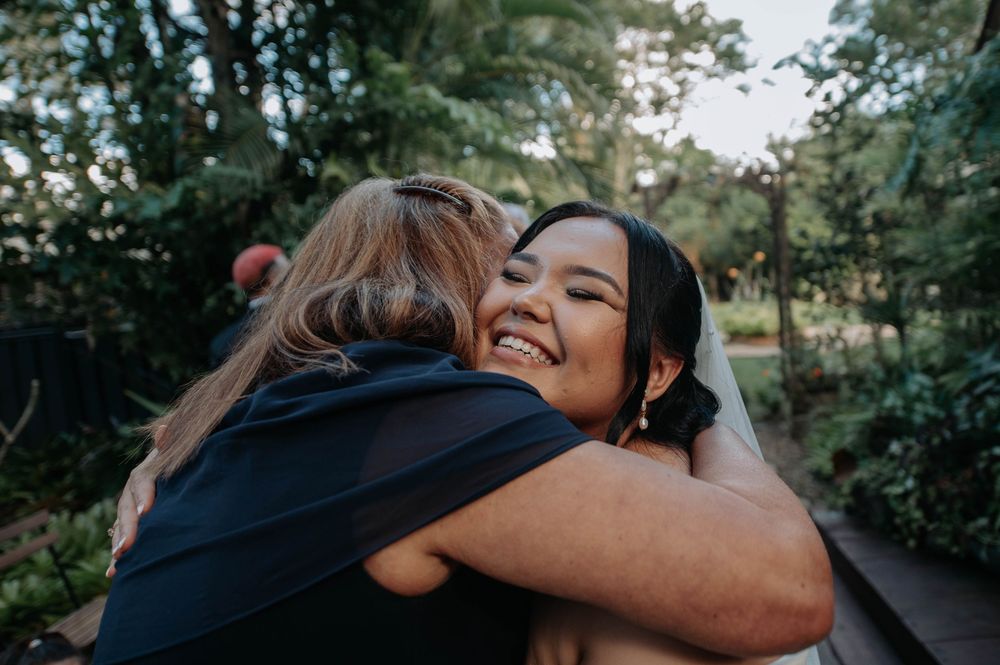 Two people embracing in a romantic moment outdoors with sunlight filtering through trees in the background.