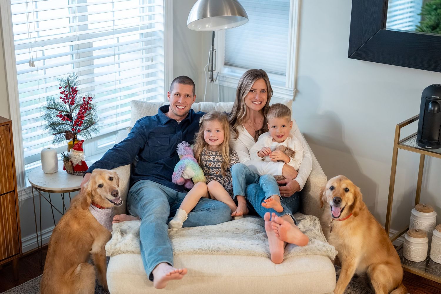 A family relaxes on a couch with their golden retriever while watching TV in their living room.