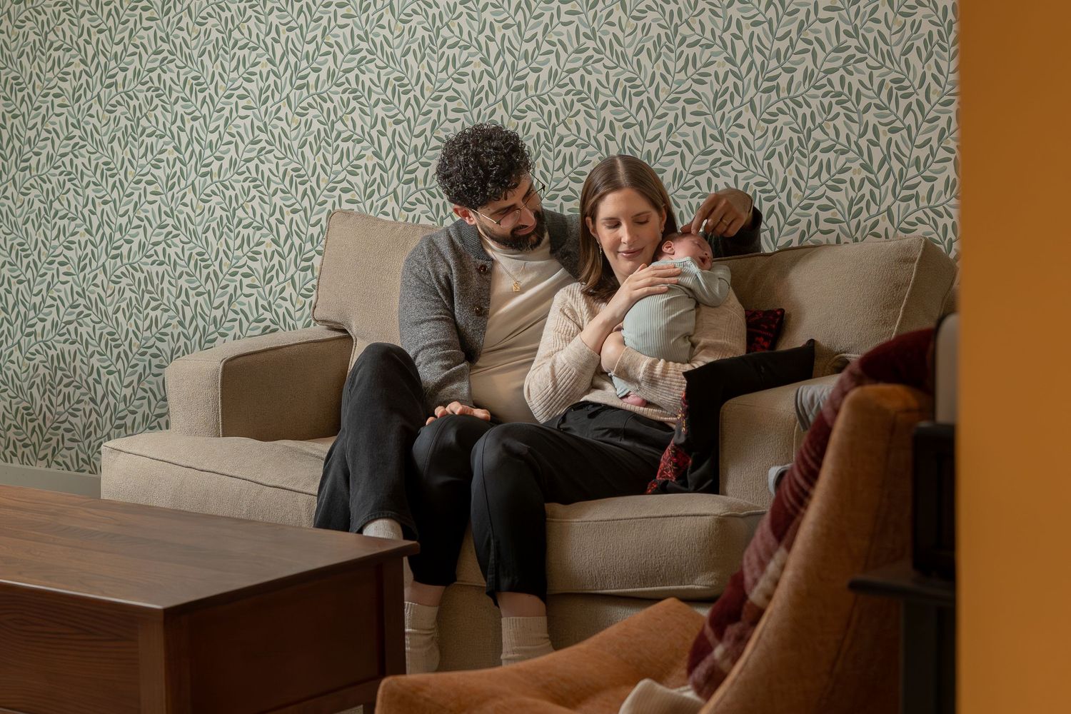Two people sit close together on a couch at home while looking at a mobile device in their hands.