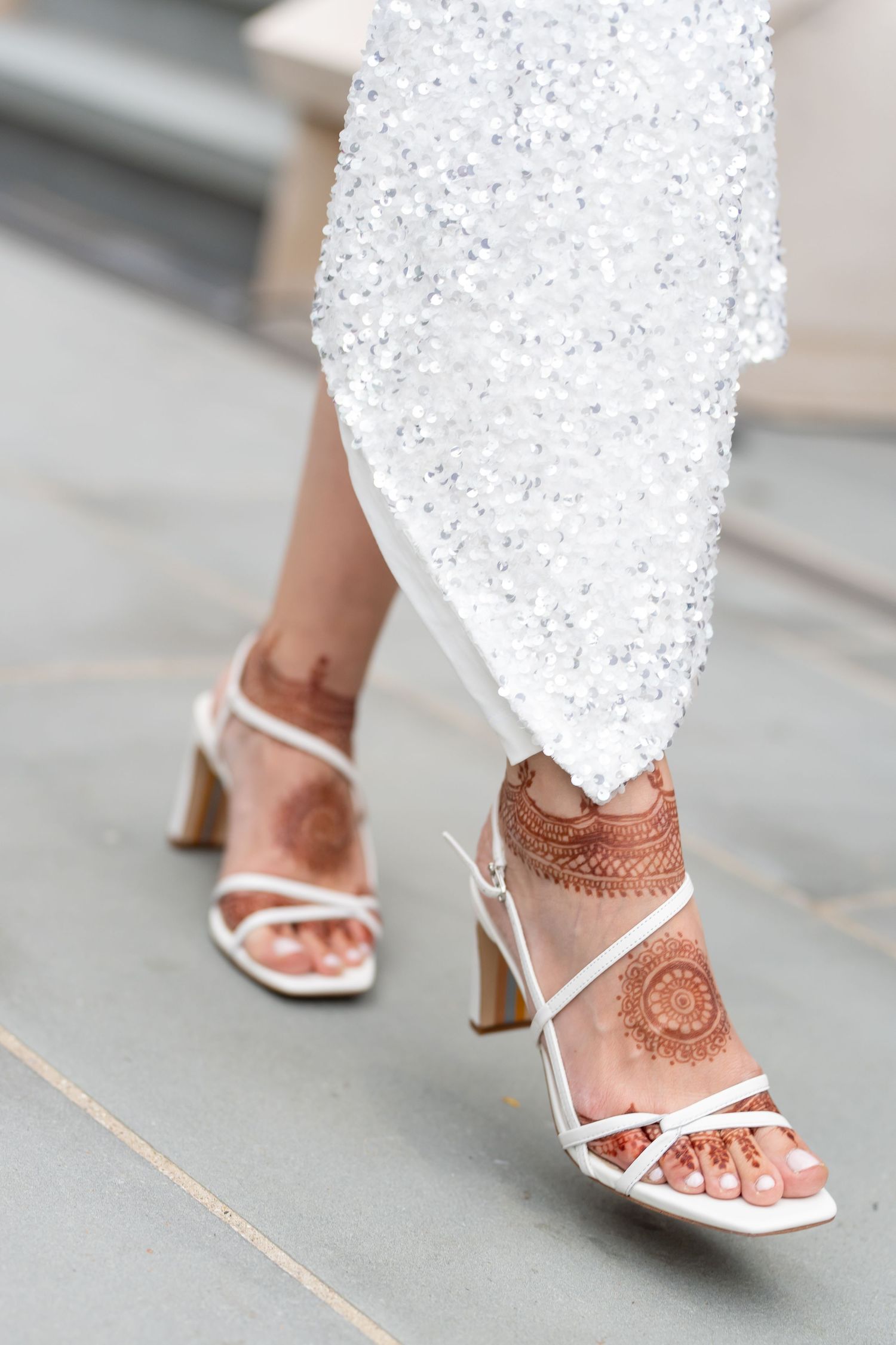 Woman walking in white dress and brown strappy heeled sandals on grey pavement.