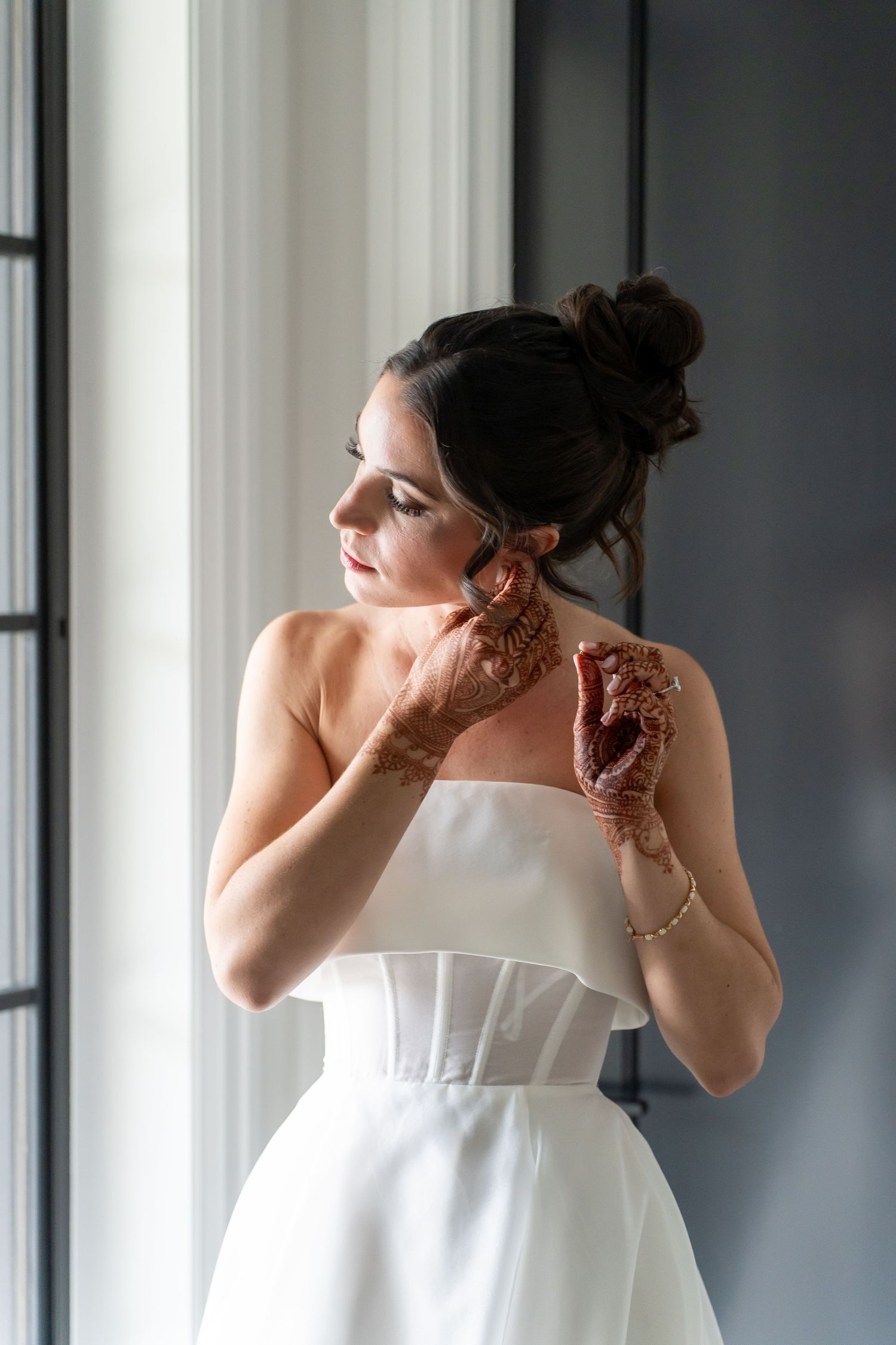 Person in a strapless white wedding dress getting ready near windows in natural light.