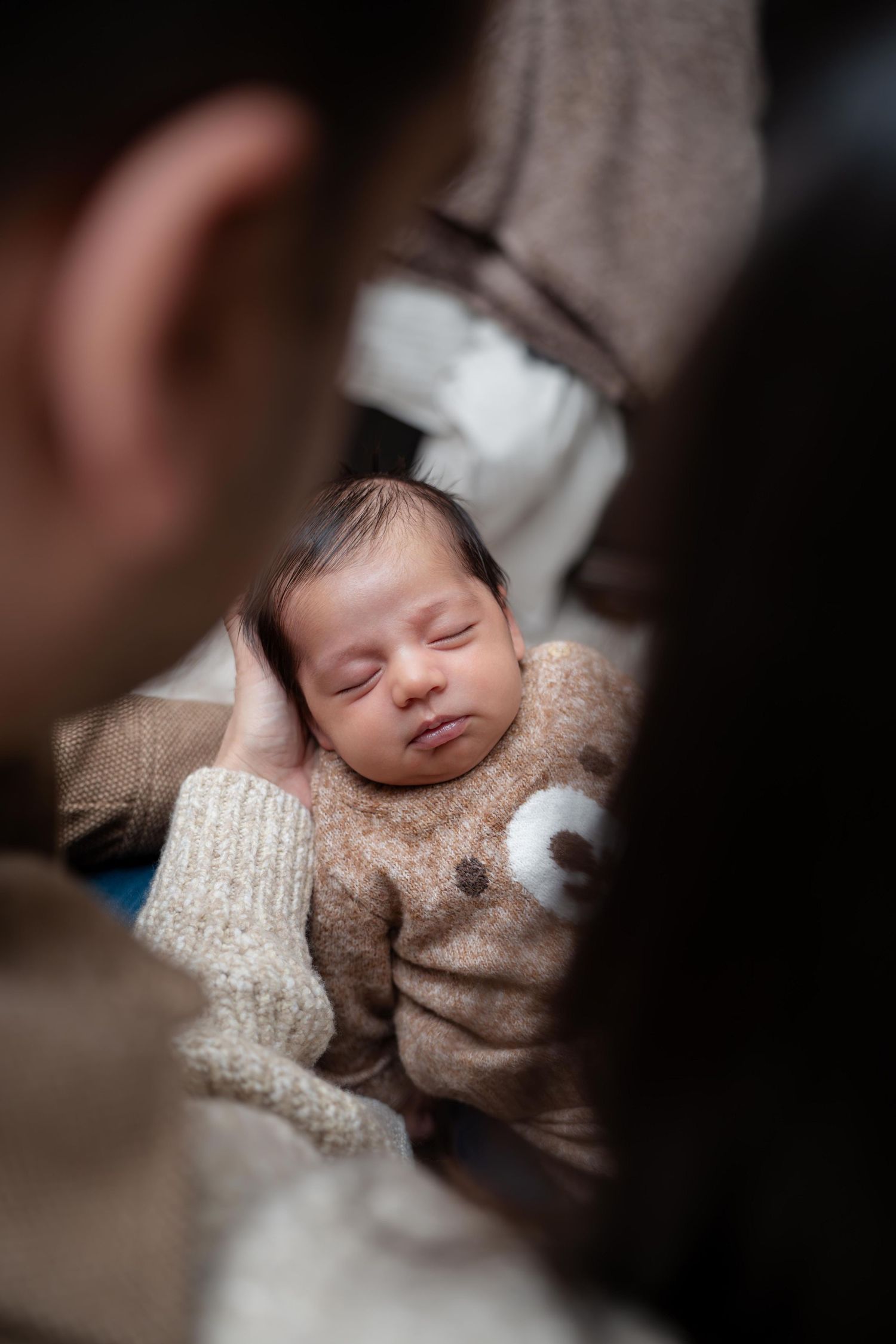 A sleeping newborn baby wearing a cozy beige knit sweater rests peacefully on soft fabric.